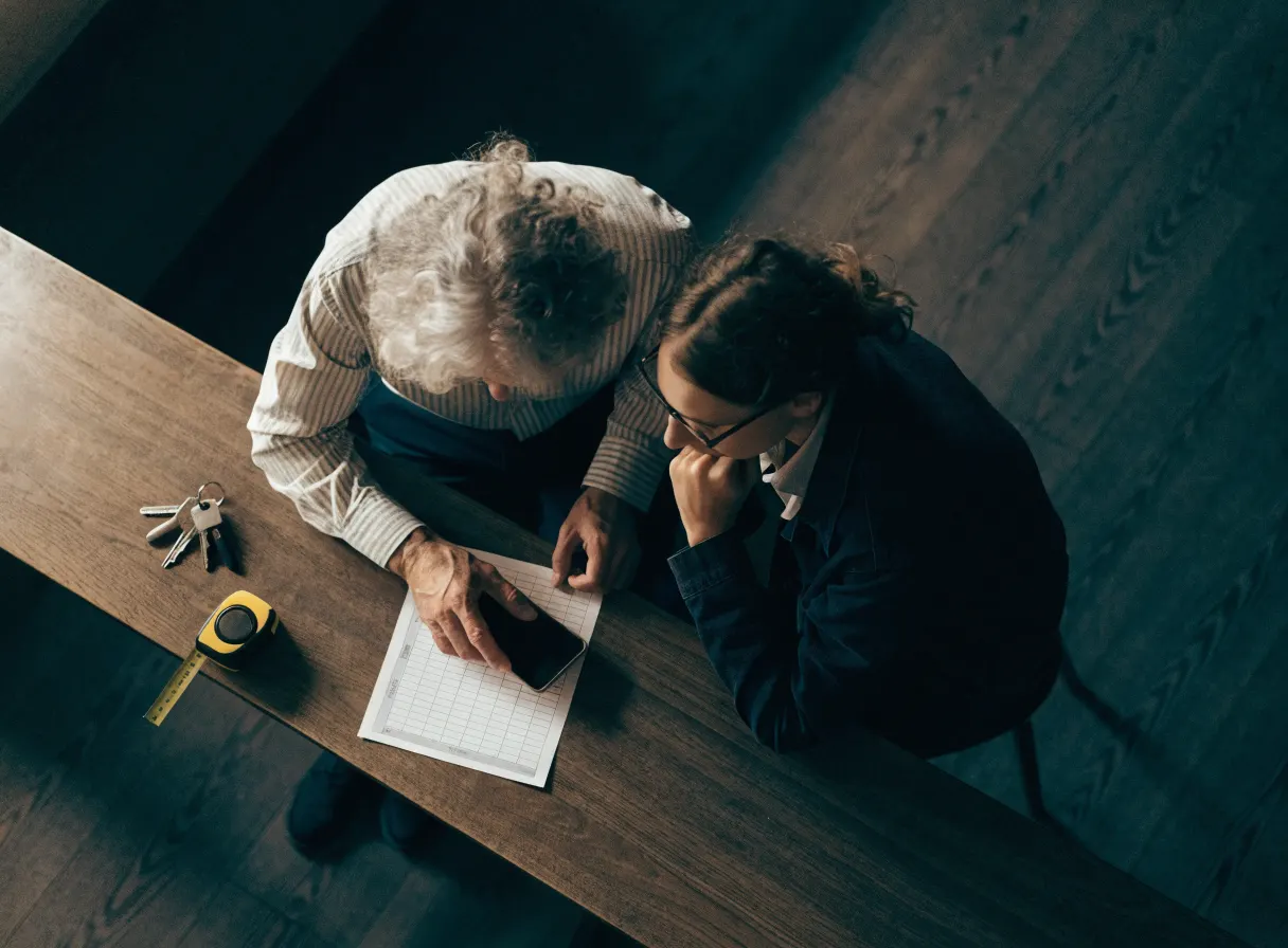 An owner and a tenant reviewing a checklist at a wooden counter, keys and a tape measure beside them